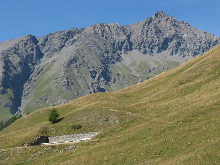 Abbiamo appena parcheggiato l'auto e già si intravede la parte superioire della casermatta LX.Si può notare sullo sfondo la cima della Pierre Menue davvero imponente con i suoi 3505 metri di altezza