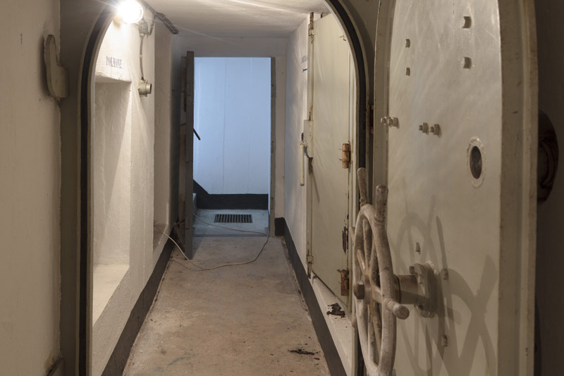 Corridoio d'ingresso. Sulla destra, prima la botola imbullonata del locale polmone, più lontana la porta del locale gruppo elettrogeno. Sulla sinistra, il deposito carburanti.