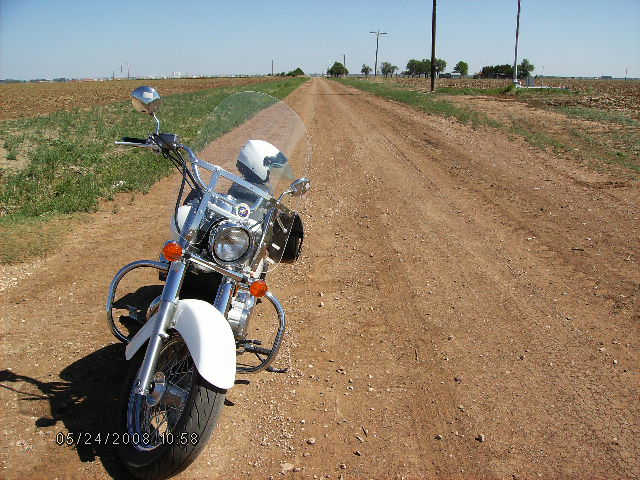 una moto, uno zaino, un casco, un Cappello Alpino e tanta polvere